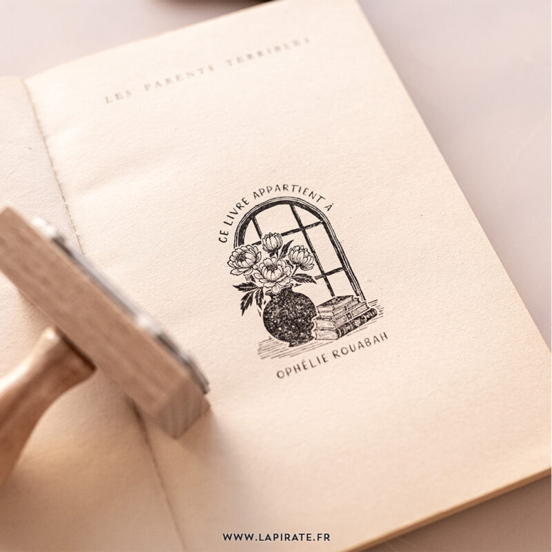 Tampon ex-libris personnalisable avec illustration d'un bouquet de pivoines dans un vase posé devant une fenêtre à carreaux, accompagné d'une pile de livres, créant une ambiance de jardin secret littéraire - Ex libris à personnaliser, idée cadeau originale - La Pirate