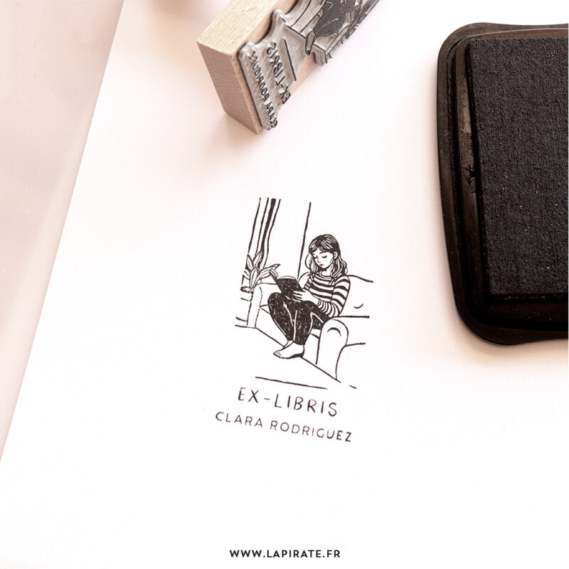 Tampon ex-libris jeune fille en marinière lisant confortablement sur un canapé, lecture cocooning. Tampon livre personnalisé. Idée cadeau originale à offrir pour enfant amoureux de lecture - La Pirate